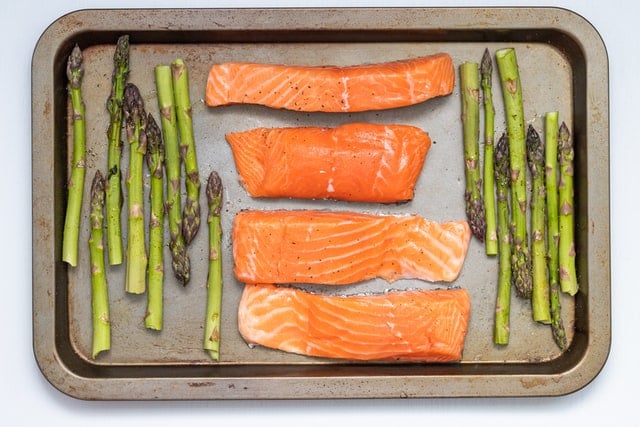 raw salmon and asparagus placed on baking tray